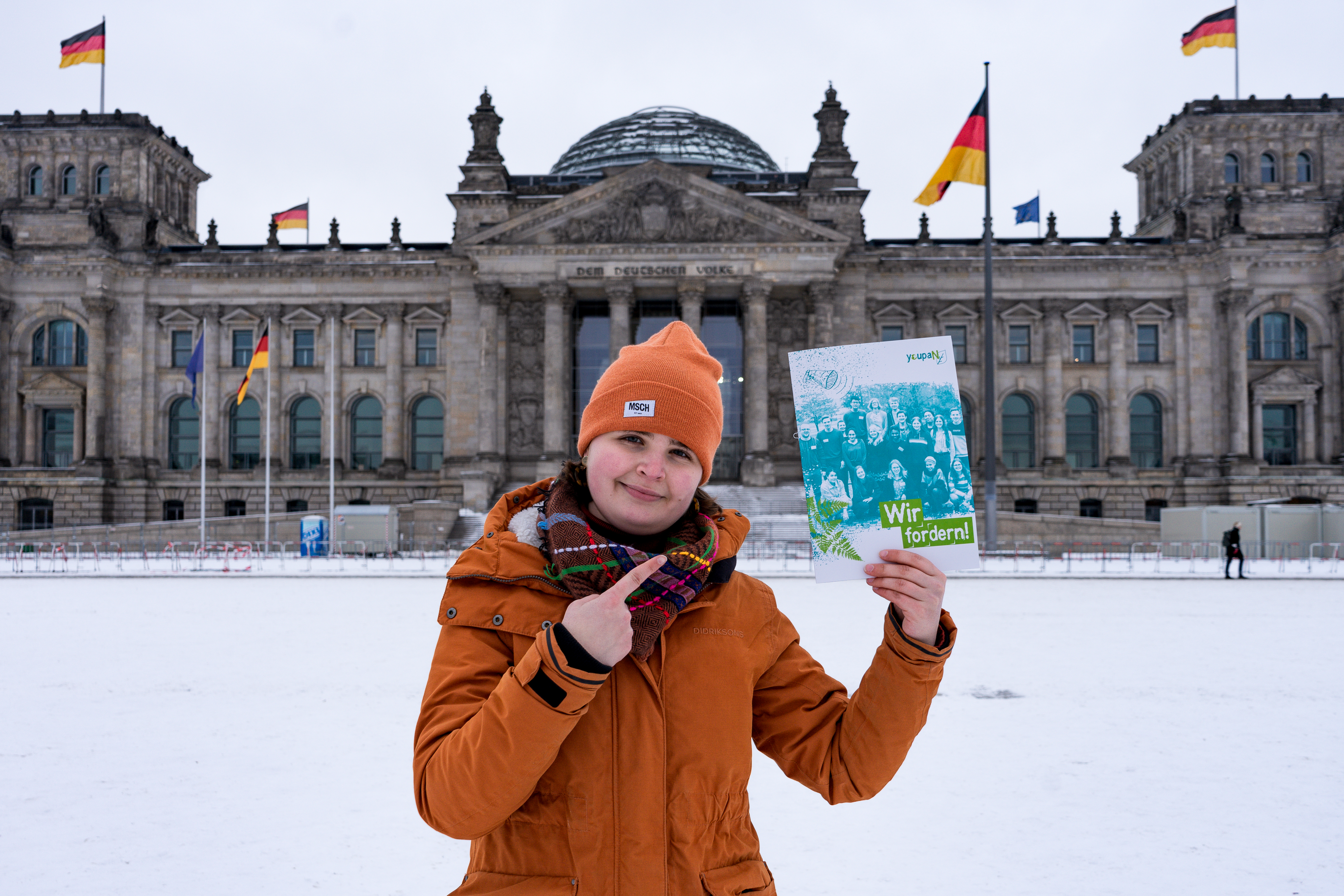 Amelie Paassen hält vor dem Bundestagsgebäude die youpaN-Forderungsbroschüre hoch.