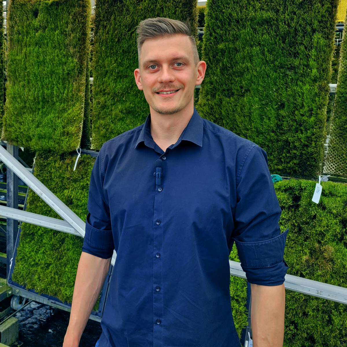 Peter Sänger in blauem Hemd steht lächelnd vor einer Wand aus Platten, die mit Moos bepflanzt sind.